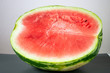 Half of big green watermelon with ripe red flesh on table