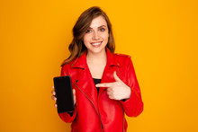 Closeup Photo Of Girl Pointing Black Phone Isolated Over The Yellow Background