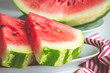 Close up of triangular slices of ripe watermelon with red flesh served on white plate with striped napkin