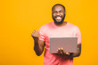 I'm winner! Excited happy afro american man looking at laptop computer screen and celebrating the win isolated over yellow background.