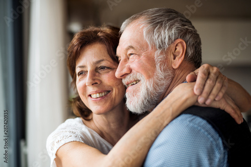 A senior couple indoors at home, looking out of window. Tableau sur Toile
