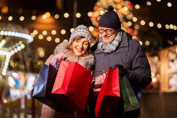 sale, winter holidays and people concept - happy senior couple with shopping bags at christmas marke