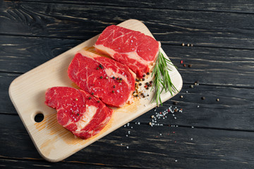 Wall Mural - Three pieces of juicy raw beef on a cutting board on a black wooden table background.