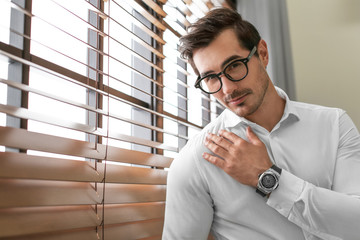 Wall Mural - Handsome young man in white shirt with glasses standing near window indoors