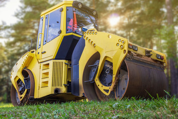 Yellow road roller on the background of forest and lawn. Yellow road roller, parked in the woods after the road repair works.  