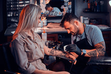 Dilligent Focused Tattoo Artist Is Creating New Tattoo On Young Woman's Hand At Tatoo Studio.