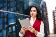 © ZoFot - Female professional financier checking e-mail on portable touch pad while standing outside company. Female entrepreneur using digital tablet for char, standing near business centre during break at job