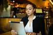 © ZoFot - Serious woman university student using touch pad for online learning while sitting in restaurant after lectures. Confident female manager reading financial news via digital tablet. Online banking