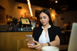 © ZoFot - Young successful businesswoman reading e-mail on mobile phone while sitting in restaurant during break at job. Confident female lawyer searching contact on cell telephone
