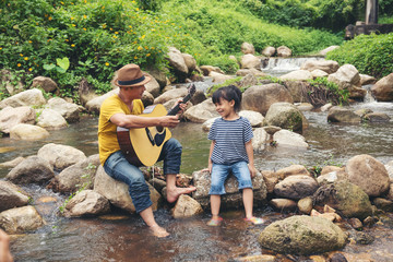 Wall Mural - Portrait of family asia man and little girl play guitar at nature Stream water.