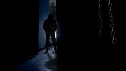 Canvas Print - hooded man behind opening door 4k loop features a dark room with hanging chains swinging and a door 