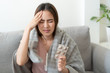 © sorrapongs - Asian Cute of  girl having headache and high temperature from illness holding pill of medicine sitting on sofa at home, Health and illness concepts