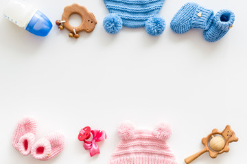 Blue and pink knitted footwear, hat, dummy, rattle and bottle frame for baby on white background top view mockup