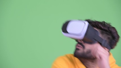 Wall Mural - Face of young overweight bearded Indian man using virtual reality headset and looking surprised