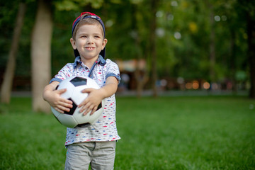 Wall Mural - Little child hand holding football and playing soccer on grass with copy space.