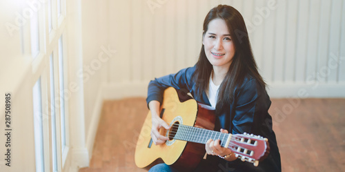 Beautiful middle-aged woman playing guitar in comfortable room Fototapet