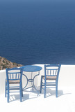 Fototapeta Do akwarium - Greece, the island of Sikinos. Two traditional taverna chairs and a blue table. In the background, the  blue Aegean sea. Picture taken at a cafe high above the waters. Peace, simplicity and nature.