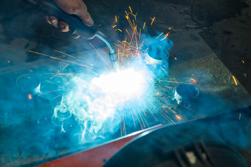 Canvas Print - Semi-automatic spot welding of metal parts during the work of the master in the construction workshop with blue smoke and yellow sparks.