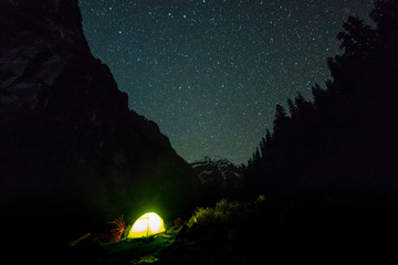 campfire under night sky with star on top of mountain surrounded by forest