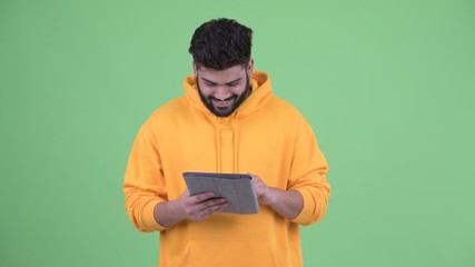 Wall Mural - Happy young overweight bearded Indian man using digital tablet