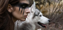 Close-up Portrait Of A Woman Hunter With War Paint On Her Cheeks Against The Backdrop Of A Wolf Face