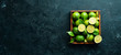 Green lime in a wooden box. Citrus fruits. On a black stone background. Top view. Free space for your text.