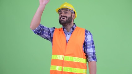 Wall Mural - Happy young overweight bearded Indian man construction worker waving hand