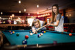 © RomanR - Beautiful woman with her friend playing billiard in pub