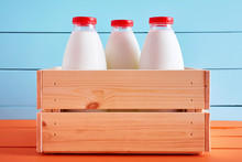 Traditional Milk Bottles In A Wooden Crate On Wooden Kitchen Table With Blue Wooden Background.