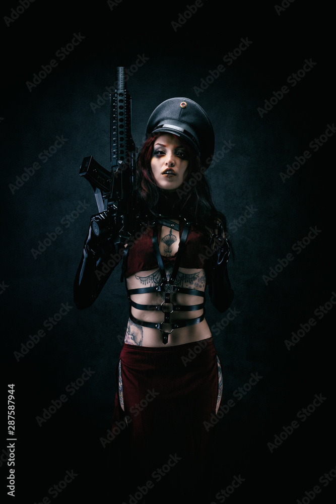 Young black-eyed Cyborg in leather armor and a cap holding a machine gun in his hands - obrazy, fototapety, plakaty 