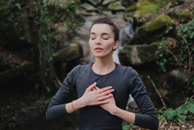 Young Woman Practicing Breathing Yoga Pranayama Outdoors In Moss Forest On Background Of Waterfall. Unity With Nature Concept.