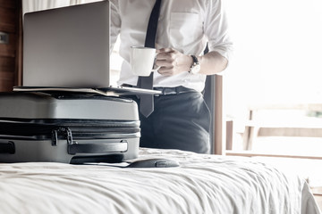 Businessman holding coffee and work on laptop in hotel room on business trip.