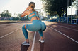 Back side view of attractive athlete girl in stylish sportswear squatting with rubber band on stadium