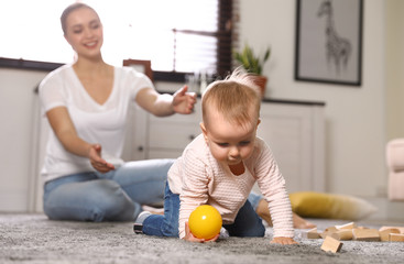 Wall Mural - Mother watching her baby crawl on floor at home