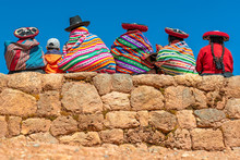 A Group Of Quechua Indigenous Women In Traditional Clothing And A Young Boy Sitting And Chatting On An Ancient Inca Wall In The Archaeological Site Of Chinchero In The Region Of Cusco City, Peru.