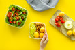 Lunch box for food to go with healthy meal in hands on yellow background top view