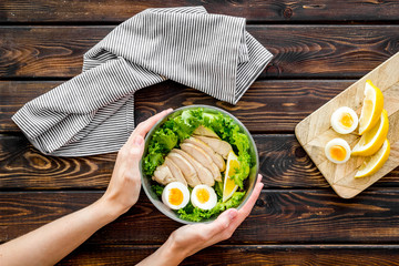 Wall Mural - Salad bowl with healthy food in hands on wooden background top view