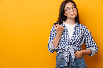 Poster - Concentrated thinking young cute teenage girl in glasses posing isolated over yellow wall background play with hair.