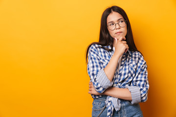 Sticker - Thoughtful serious young cute teenage girl in glasses posing isolated over yellow wall background.