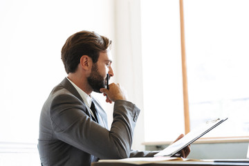 Wall Mural - Image in profile of smart focused businessman reading documents while working in office