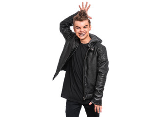 Rebellious teen boy dressed in black making horns with fingers on head, isolated on white background. Teenager in style of punk goth wearing leather jacket. Problems of transition age.