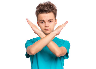 Wall Mural - Portrait of teen boy doing stop sign with crossed hands, isolated on white background. Cute caucasian young teenager making stop gesture with serious facial expression. Child looking at camera.