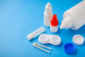 Optical corrective medical soft contact lenses for eyes in white plastic case with storage solution, accessories and care products in plastic bottles on blue background, Cleaning