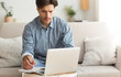 © Prostock-studio - Worried Young Man Taking Notes Using Laptop Sitting On Sofa