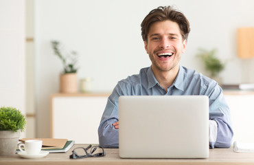 Poster - Positive Guy Laughing Looking At Camera Sitting At Laptop Indoor