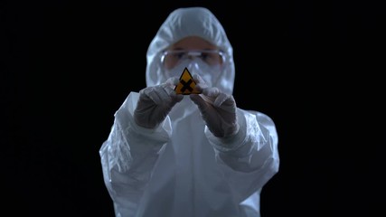 Wall Mural - Lab worker in protective suit showing cross symbol against dark background