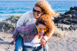 © simona - DIversity and friendship concept with people couple of women having fun together carrying each other and laughing a lot in outdoor leisure activity - blue ocean in background