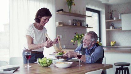 Wall Mural - Senior couple in love serving lunch indoors at home, talking.