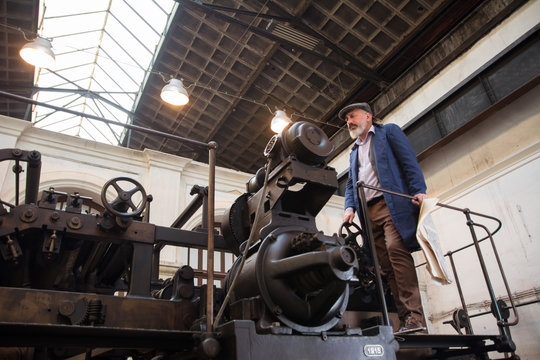 Worker standing on top platform of an old vintage press for newspaper printing