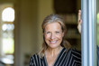 © Westend61 - Portrait of smiling mature woman standing at opened terrace door